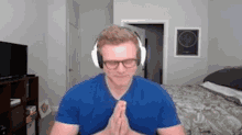 a man wearing headphones and glasses is praying in front of a camera .