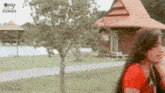 a woman in a red shirt is standing in front of a house .