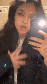 a woman is taking a selfie in front of a mirror with her cell phone .