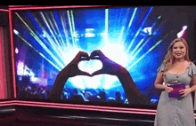 a woman is making a heart shape with her hands in front of a screen .