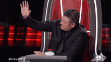 a man is sitting in a chair with his hand in the air and the words #thevoice on the bottom