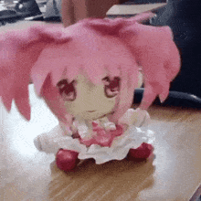a stuffed doll with pink hair is sitting on a table .