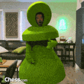 a man in a green chess costume is standing in front of a chess.com logo