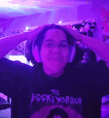 a person wearing headphones and a rocky horror shirt holds their head