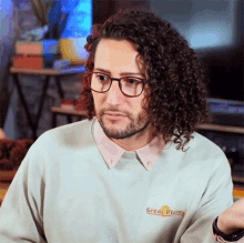 a man with curly hair and glasses is wearing a sweater that says great plains on it .