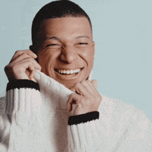 a man wearing a white sweater is smiling and covering his face with his hands