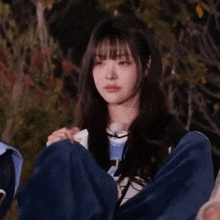 a girl with long hair and bangs is giving a thumbs up sign while wrapped in a blue blanket .