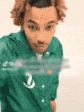 a young man with curly hair is wearing a green shirt that says tiktok