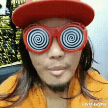 a man wearing a red hat and hypnotic glasses is making a funny face .