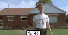 a man in a white shirt is standing in front of a brick house with the word gmeth on his shirt .