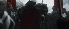 a man in armor with a red cape is standing in a crowd of people .