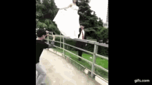 a man is taking a picture of a bride in a wedding dress while standing on a bridge .