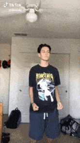 a young man wearing a pokemon shirt is standing in a room with a ceiling fan