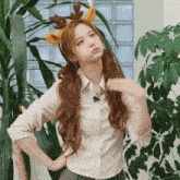 a woman wearing a reindeer headband is standing next to a plant