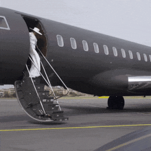 a woman in a white dress climbs the stairs of an airplane
