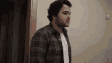 a man wearing a plaid shirt and a white shirt is standing in a room .