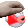 a hand is holding a red and white cartoon character with a red nose .
