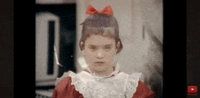 a little girl with a red bow in her hair is looking at the camera with a youtube play button below her