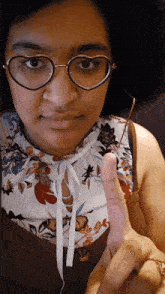 a woman wearing glasses and a floral top holds a pink object in her hand