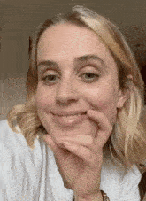 a woman with blonde hair is smiling with her hand on her chin .