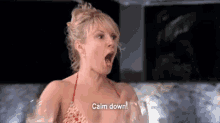 a woman in a bikini is sitting in a hot tub with her mouth open and holding a glass of wine .