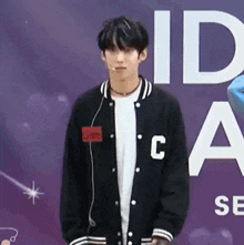 a young man wearing a baseball jacket and headphones is standing in front of a purple sign .