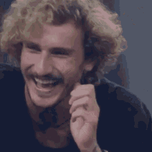 a man with curly hair and a mustache is laughing with his hand on his face .