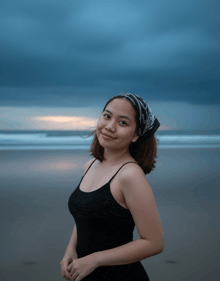 a woman wearing a black tank top and a bandana stands on a beach