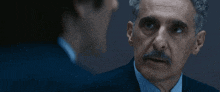 a man with a mustache is talking to another man in a suit and tie .