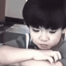 a young boy is sitting at a table with his hands on his knees and looking down .