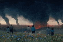 a group of people standing in a field of flowers looking at a tornado