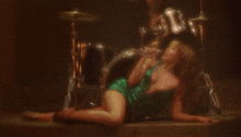 a woman in a green dress is laying on the floor in front of drums