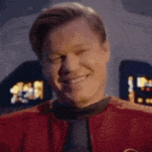 a man in a red jacket is smiling with his eyes closed in a room .