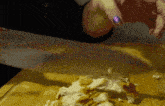 a person with purple nails is cutting a piece of food