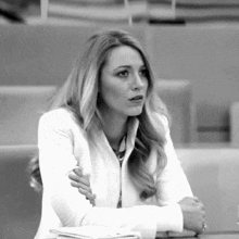 a woman in a white jacket sits at a desk with her arms crossed