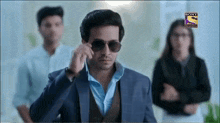 a man wearing sunglasses and a suit is standing in front of a group of people ..
