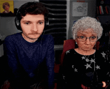 a man wearing headphones stands next to an elderly woman wearing glasses