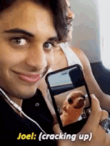 a man is holding a cell phone with a picture of a dog on it and says joel cracking up .