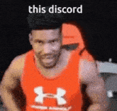 a man in a red under armour tank top is standing in front of a chair .