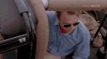 a man wearing sunglasses and a blue shirt is sitting in the back seat of a car .