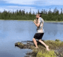 a man is standing on a rock near a lake holding a can of soda .