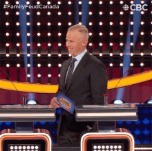 a man in a suit and tie is standing in front of a podium holding a family feud trophy