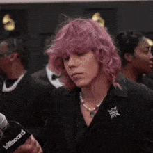 a woman with pink hair is standing in front of a microphone at a red carpet event .