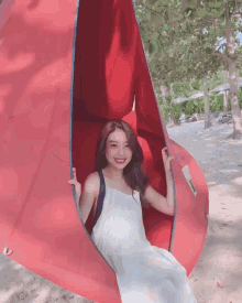 a woman in a white dress sits in a red hammock on the beach