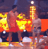 a man in a red shirt is dancing on a stage with a woman sitting on the floor .