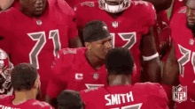a group of football players are standing in a huddle . one of the players is named smith .