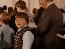 a man in a suit is putting a vest on a young boy in a crowd of people .