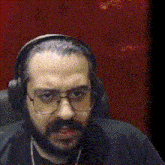 a man wearing glasses and headphones is sitting in front of a red wall
