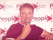 a man speaking into a microphone in front of a sign that says people meet the stars