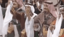 a group of men in traditional arabic clothing are standing in a crowd and dancing .